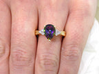 This is a women's ring with a 2.00ct pear shape mystic fire topaz center in green and purple with .12ct natural accent diamonds set in 14K yellow gold on a women's finger.