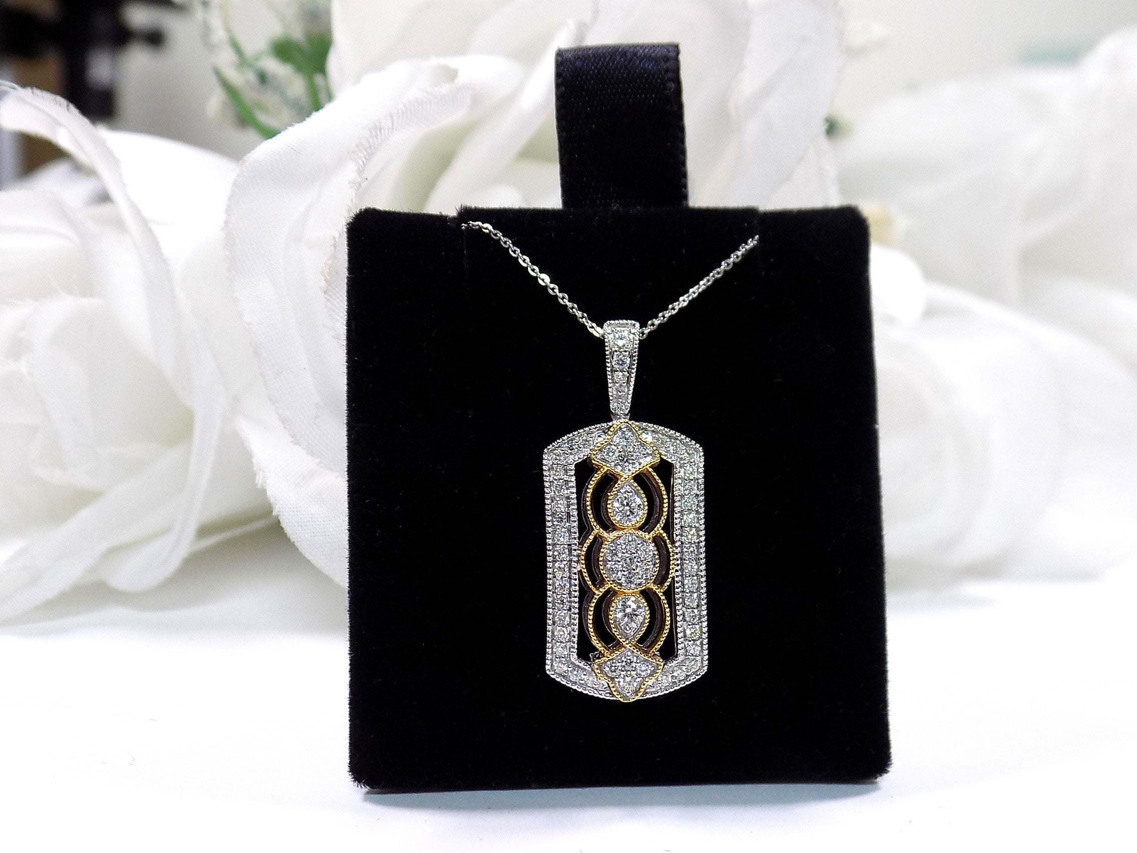 This is a .33ct natural diamond pendant that is a fiigree style in 2-tone white and yellow gold on a black pad with a white floral background.