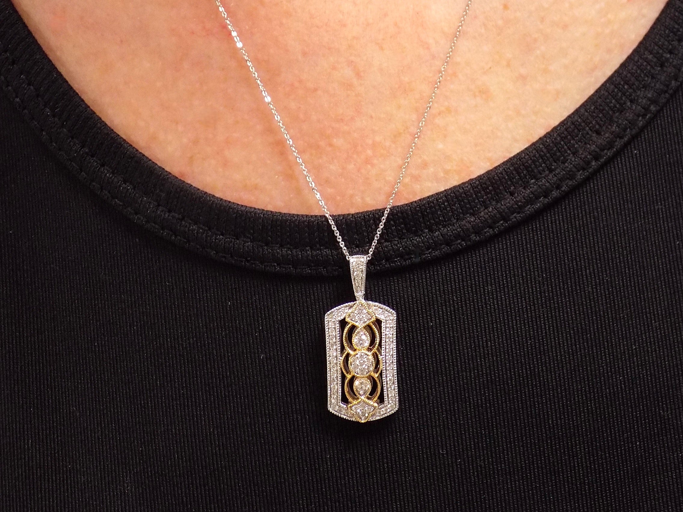This is a .33ct natural diamond pendant that is a fiigree style in 2-tone white and yellow gold on a ladies neck with a black shirt.