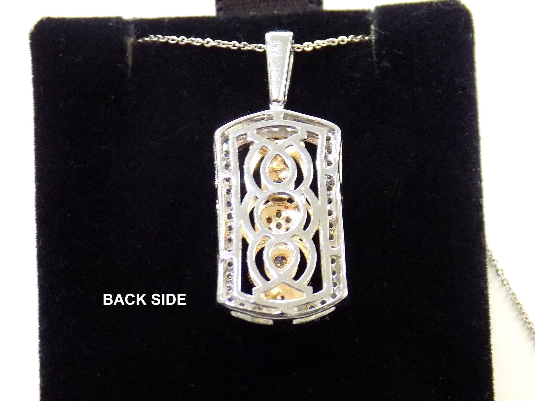This is a photo of the back side of a .33ct natural diamond pendant that is a fiigree style in 2-tone white and yellow gold on a black pad.