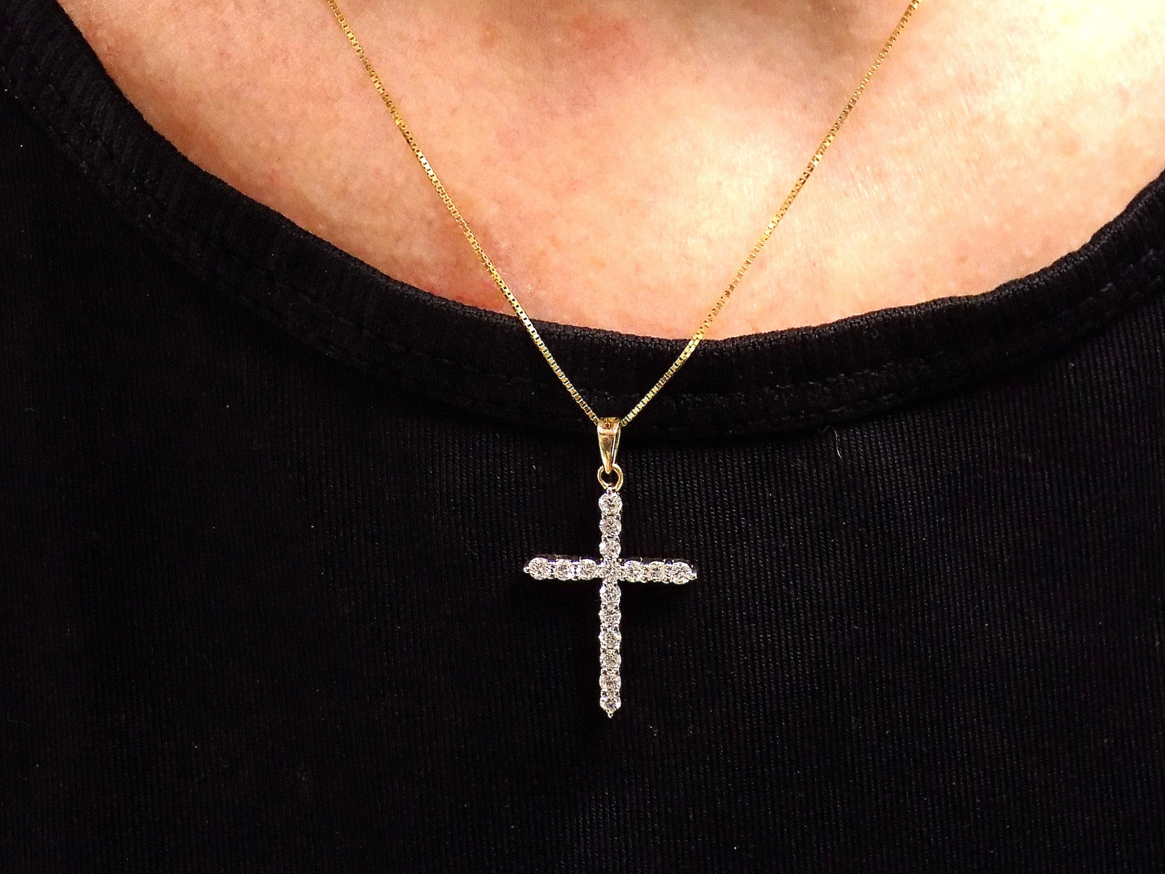 This is a .50ct natural diamond cross pendant in 14K white and yellow gold on a black pad with a white floral background.