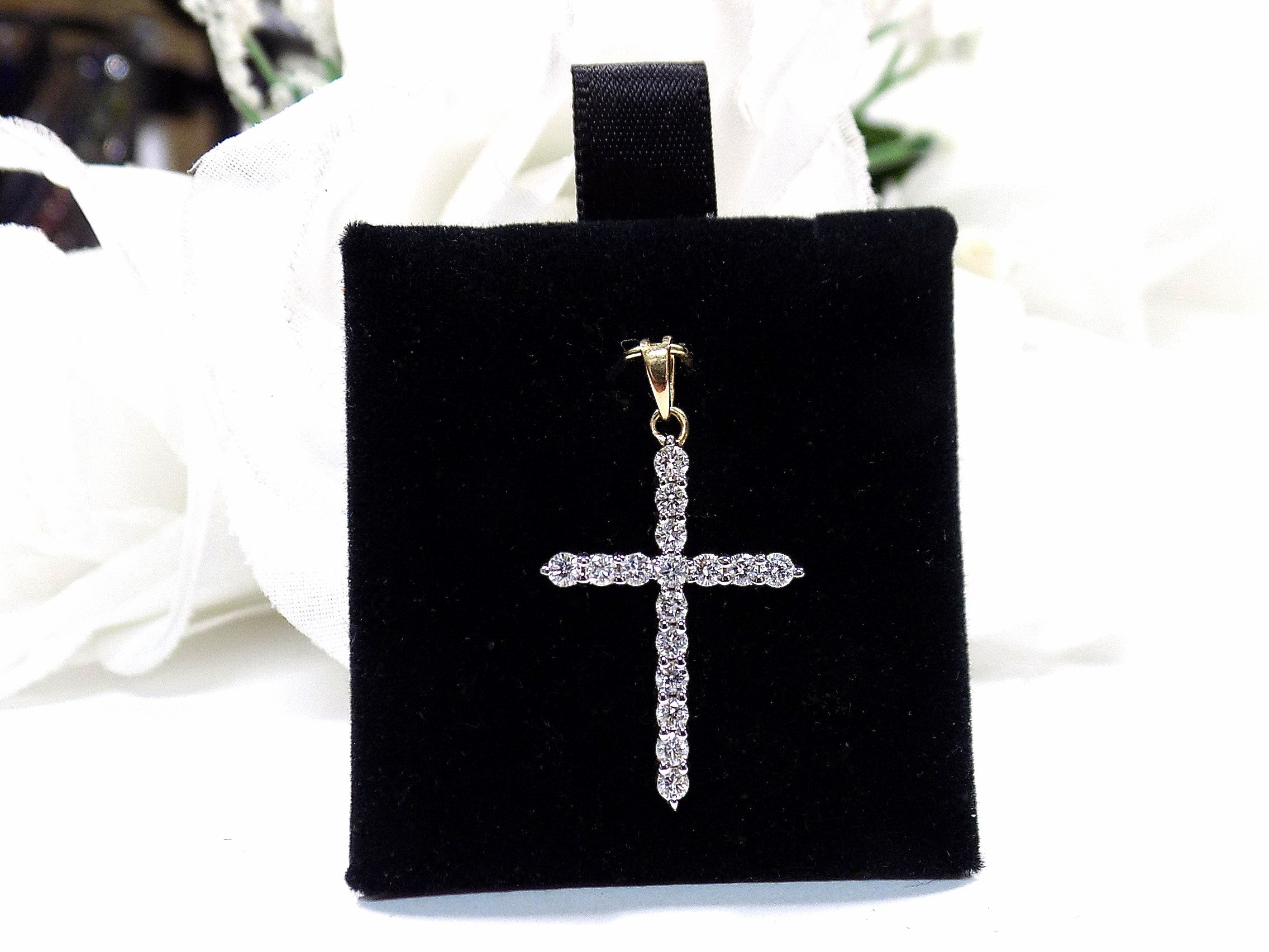 This is a .50ct natural diamond cross pendant in 14K white and yellow gold on a black pad with a white floral background.