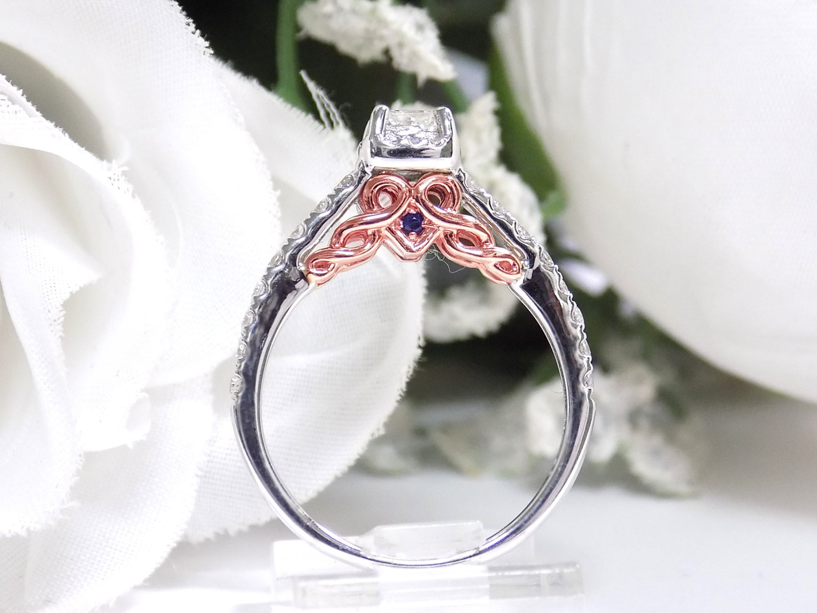 This is a side view of the engagement ring that goes with the halo style women's 2-piece wedding set highlighting the rose gold accents on the side with princess cut center weighing .88ct total in white gold with rose accents shown with white background.