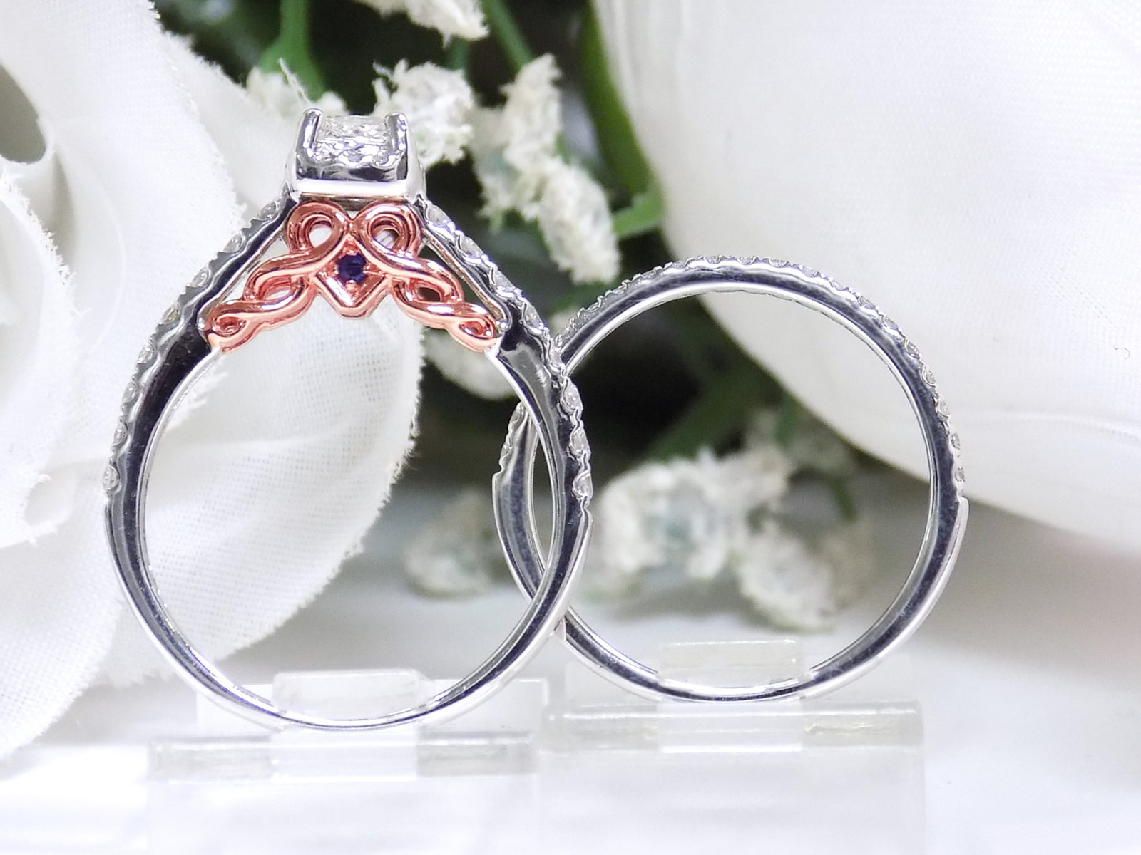 This is a side view of a halo style women's 2-piece wedding set including the engagement ring and matching band with princess cut center weighing .88ct total in white gold with rose accents shown with white background.