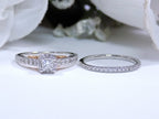 This is a halo style women's 2-piece wedding set including the engagement ring and matching band laying side by side with a princess cut center weighing .88ct total in white gold with rose accents shown with a white background.
