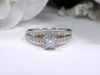 This is a halo style women's 2-piece wedding set including the engagement ring and matching band with princess cut center weighing .88ct total in white gold with rose accents shown with white background.