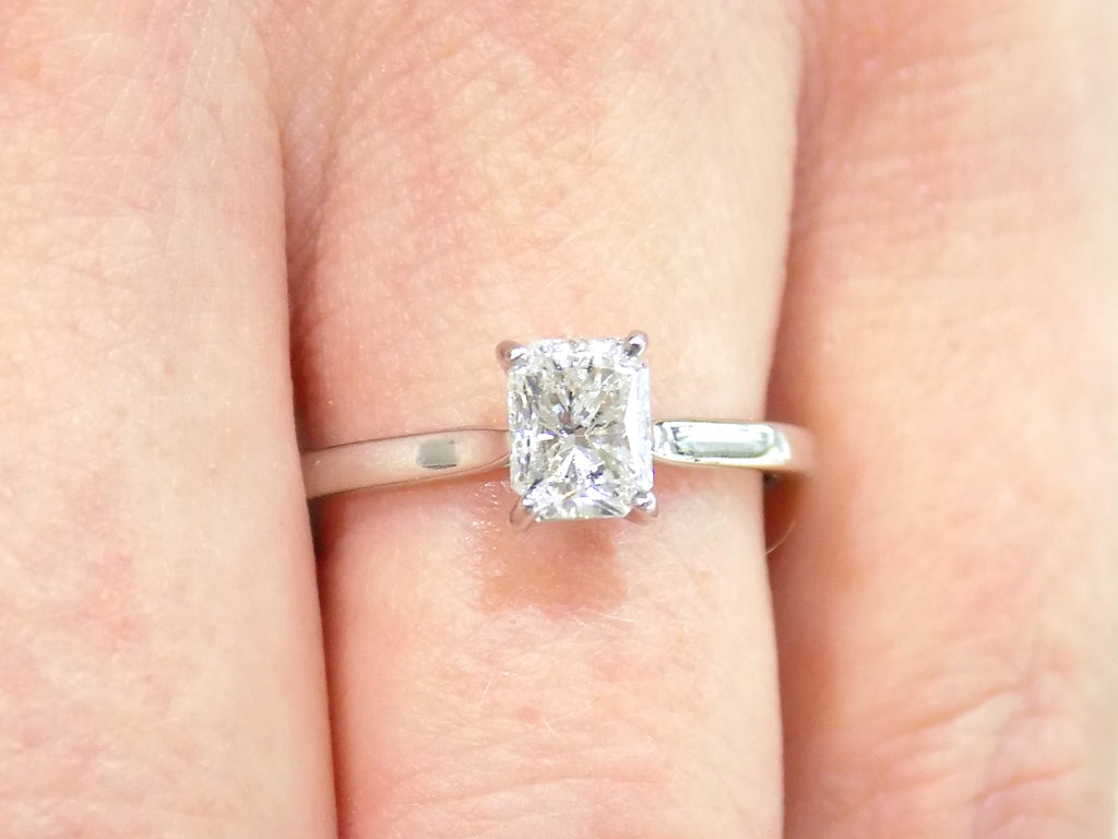 This is a women's 1.00ct natural radiant cut diamond solitaire ring in white gold shown on a woman's finger.