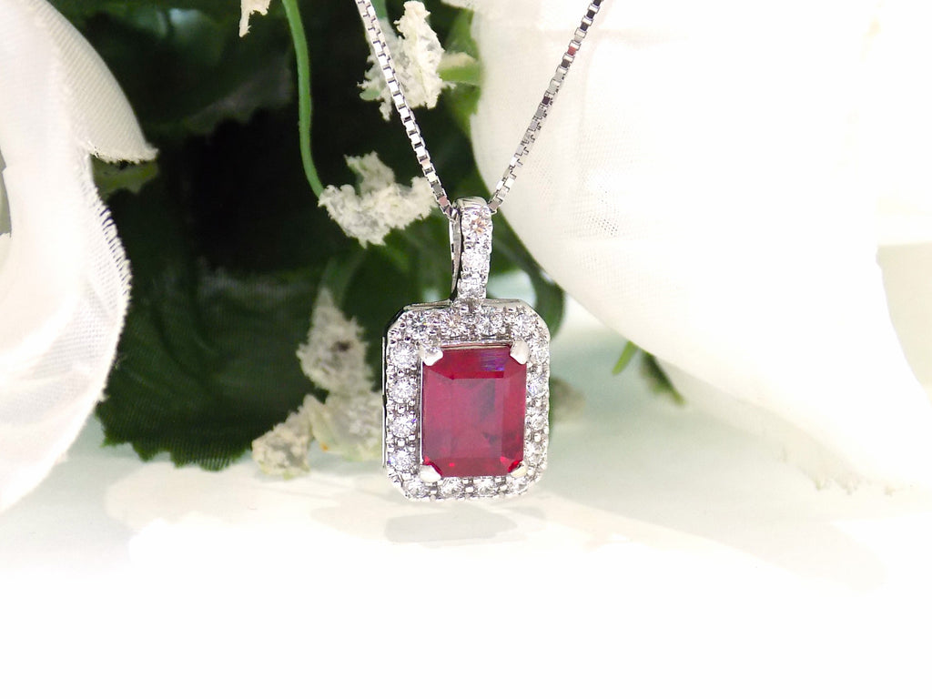 This is a women's pendant 3.65ct natural enhanced emerald cut ruby center surrounded by 1.56ct total weight in natural round diamond accents in 14K white gold.