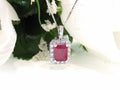 This is a women's pendant 3.65ct natural enhanced emerald cut ruby center surrounded by 1.56ct total weight in natural round diamond accents in 14K white gold.