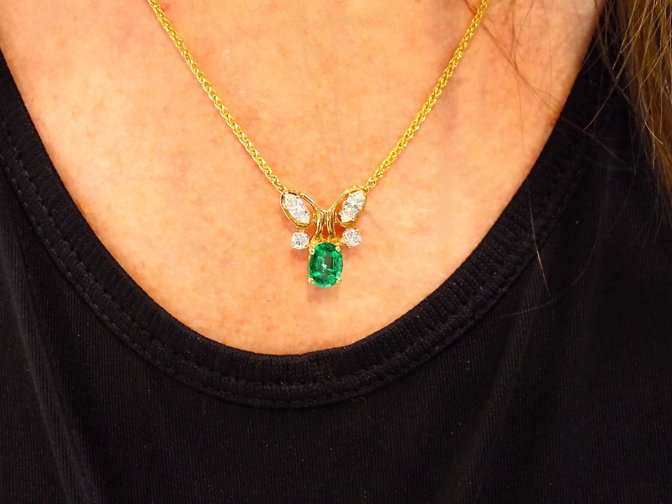 This is a women's necklace with a natural 1.00ct oval emerald and 1.00ct total weight natural marquise and round diamonds in 14K yellow gold on a women's neck.