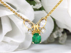 This is a women's necklace with a natural 1.00ct oval emerald and 1.00ct total weight natural marquise and round diamonds in 14K yellow gold with a white floral background.
