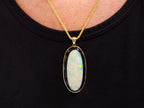 This is a women's necklace containing a 15.39ct natural crystal opal set into a black onyx background in 14K yellow gold on a women's neck with a black shirt.
