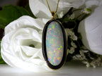 This is a women's necklace containing a 15.39ct natural crystal opal set into a black onyx background in 14K yellow gold with a white and green floral background.