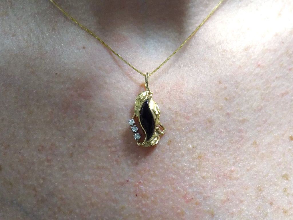 This is a genuine black onyx and diamond pendant or necklace in yellow gold shown on a woman's neck.