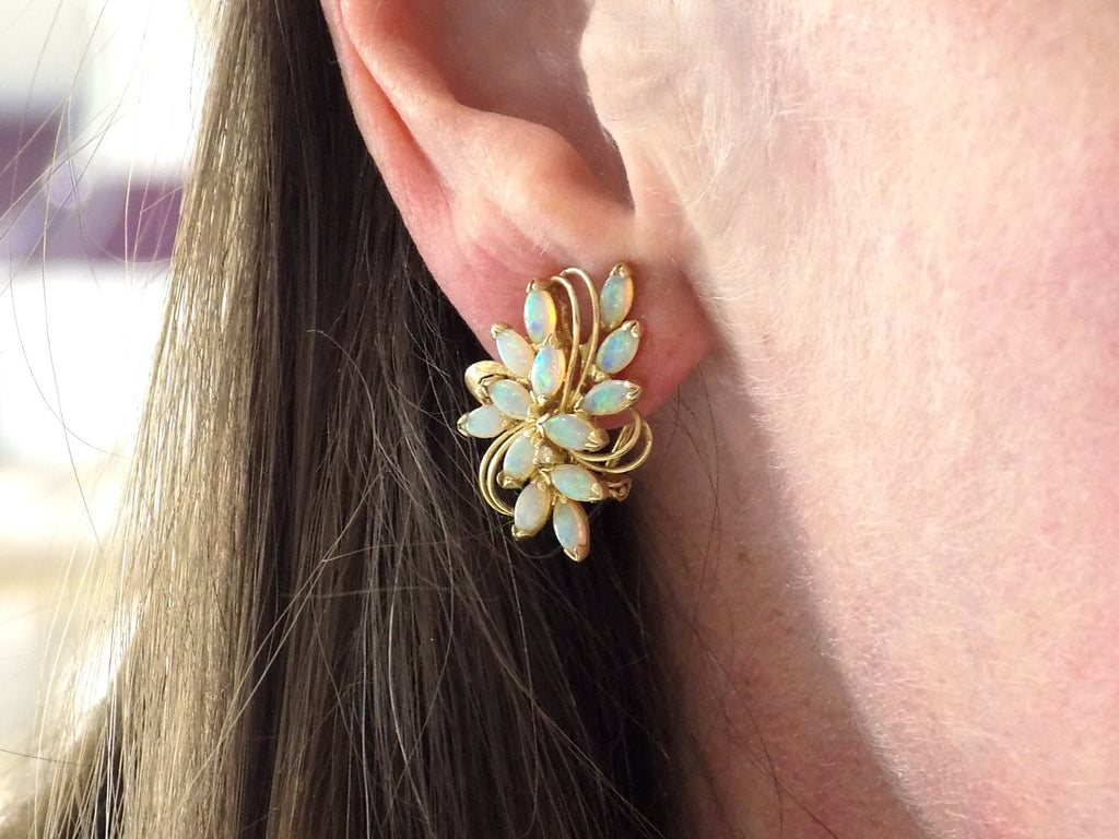 These are a pair of genuine marquise shape opal cluster earrings with omega backs in yellow gold shown in a woman's ear.