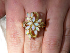 This is a cluster of 12 genuine marquise shaped opals in a yellow gold ring shown on a woman's finger.