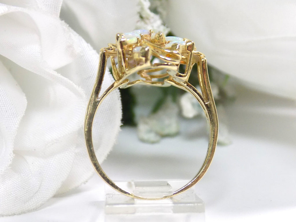 This is a side view of a cluster of 12 genuine marquise shaped opals in a yellow gold ring shown with a white flowery background.
