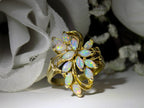 This is a cluster of 12 genuine marquise shaped opals in a yellow gold ring shown with a white flowery background.