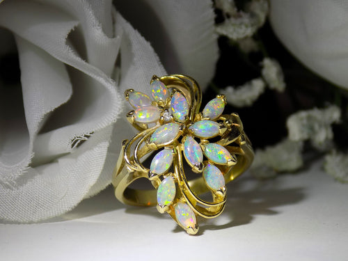 This is a cluster of 12 genuine marquise shaped opals in a yellow gold ring shown with a white flowery background.