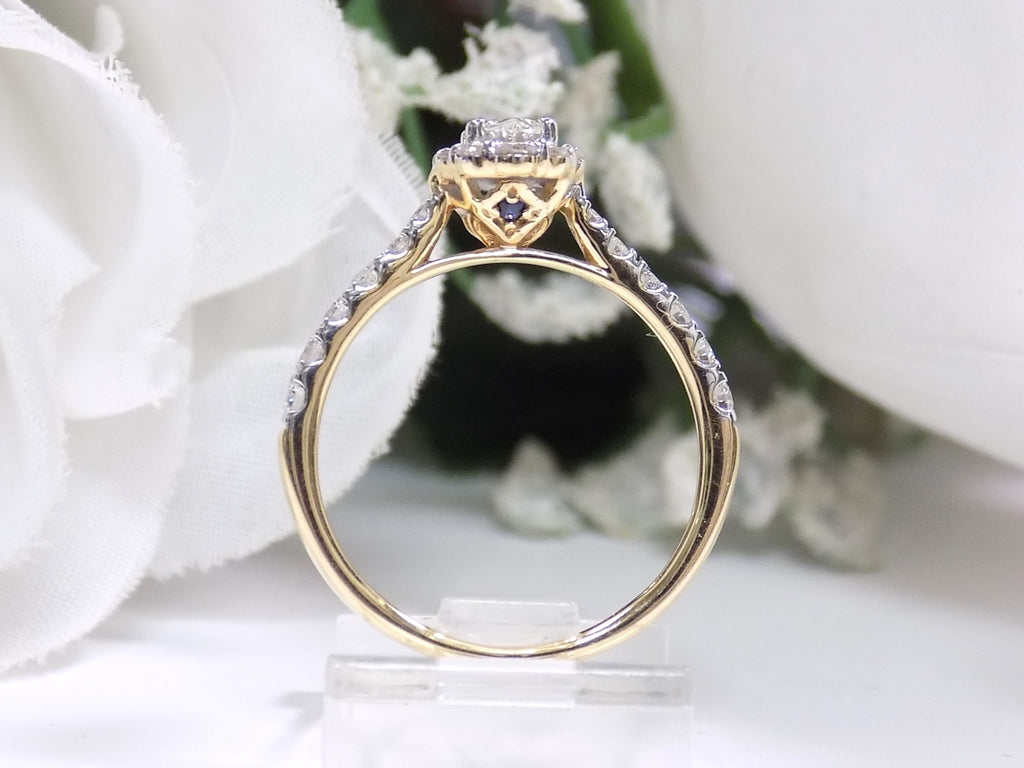 This is a side view of a oval shape diamond engagement ring in yellow gold with white gold prongs and a white background.