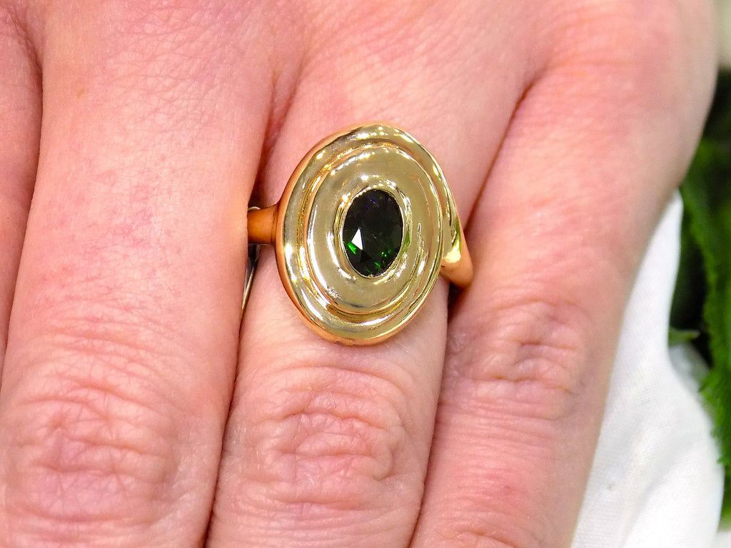 This is a women's estate ring with a .90ct oval green colored Tsavorite set in 14K yellow gold on a women's finger.