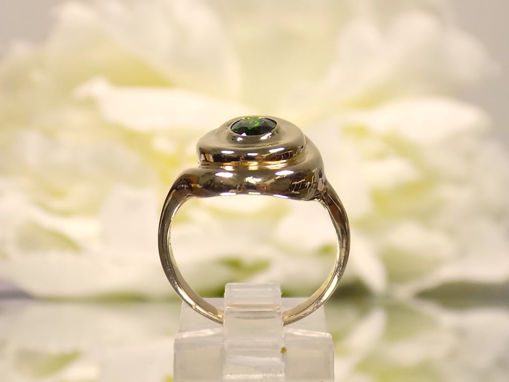 This is a women's estate ring with a .90ct oval green colored Tsavorite set in 14K yellow gold with a white floral background in a side view.
