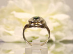This is a women's estate ring with a .90ct oval green colored Tsavorite set in 14K yellow gold with a white floral background in a side view.