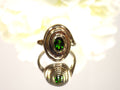 This is a women's estate ring with a .90ct oval green colored Tsavorite set in 14K yellow gold with a white floral background.