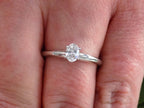 This is a white gold natural oval shape diamond solitaire shown on a woman's finger.