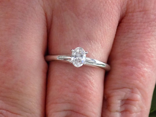 This is a white gold natural oval shape diamond solitaire shown on a woman's finger.