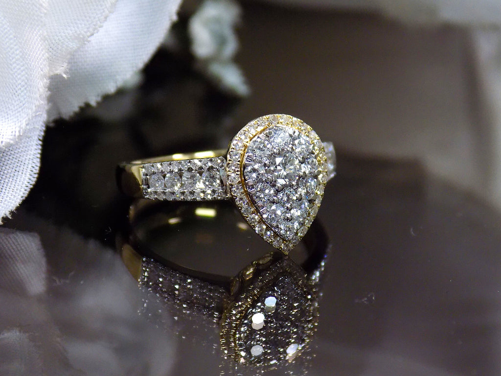 This is a .75ct total weight pear shape natural diamond cluster ring in two tone white and yellow gold on a black background.