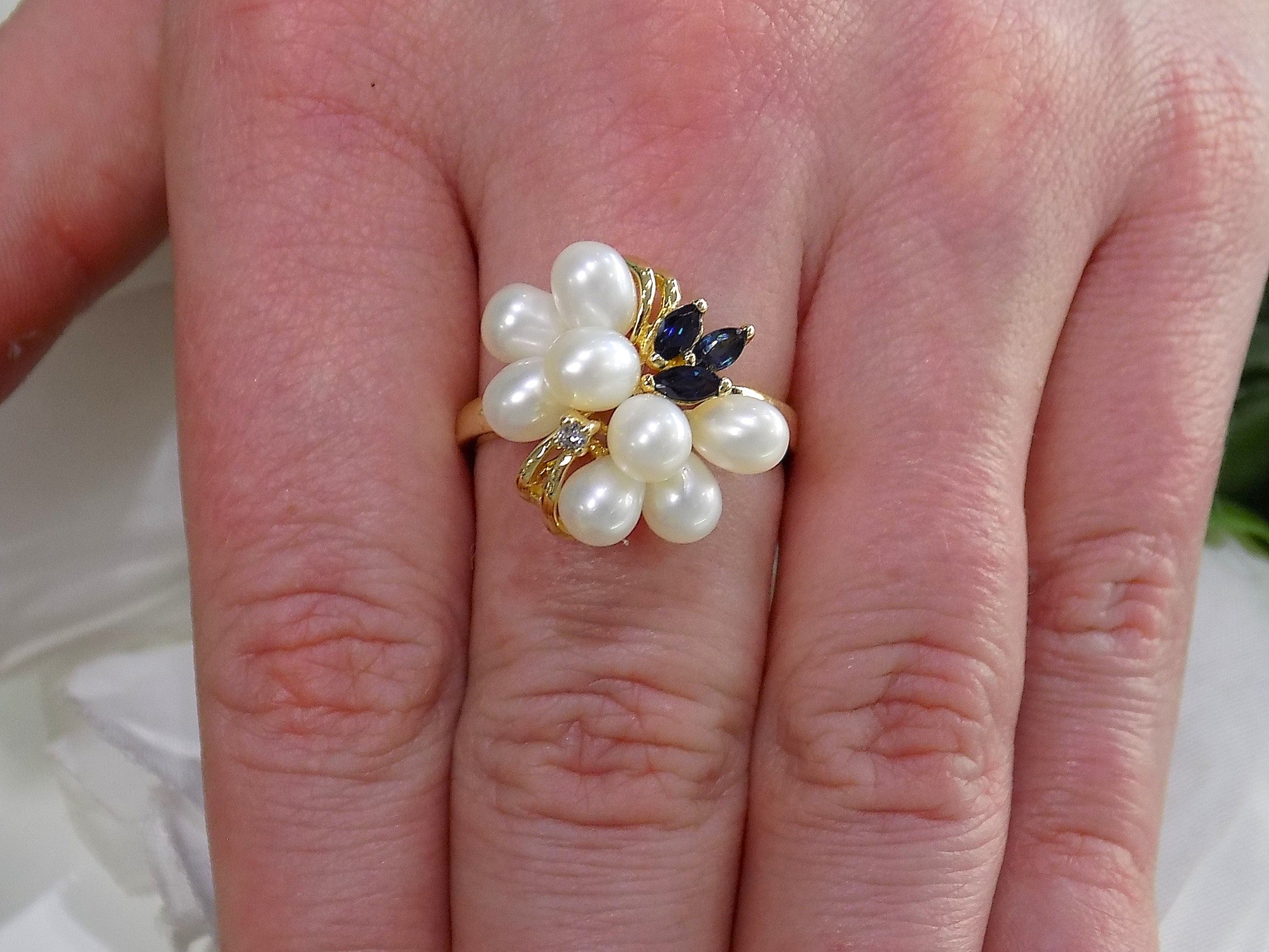 This is a freshwater pearl, blue sapphire, and diamond ring in yellow gold from our estate collection shown on a woman's finger.