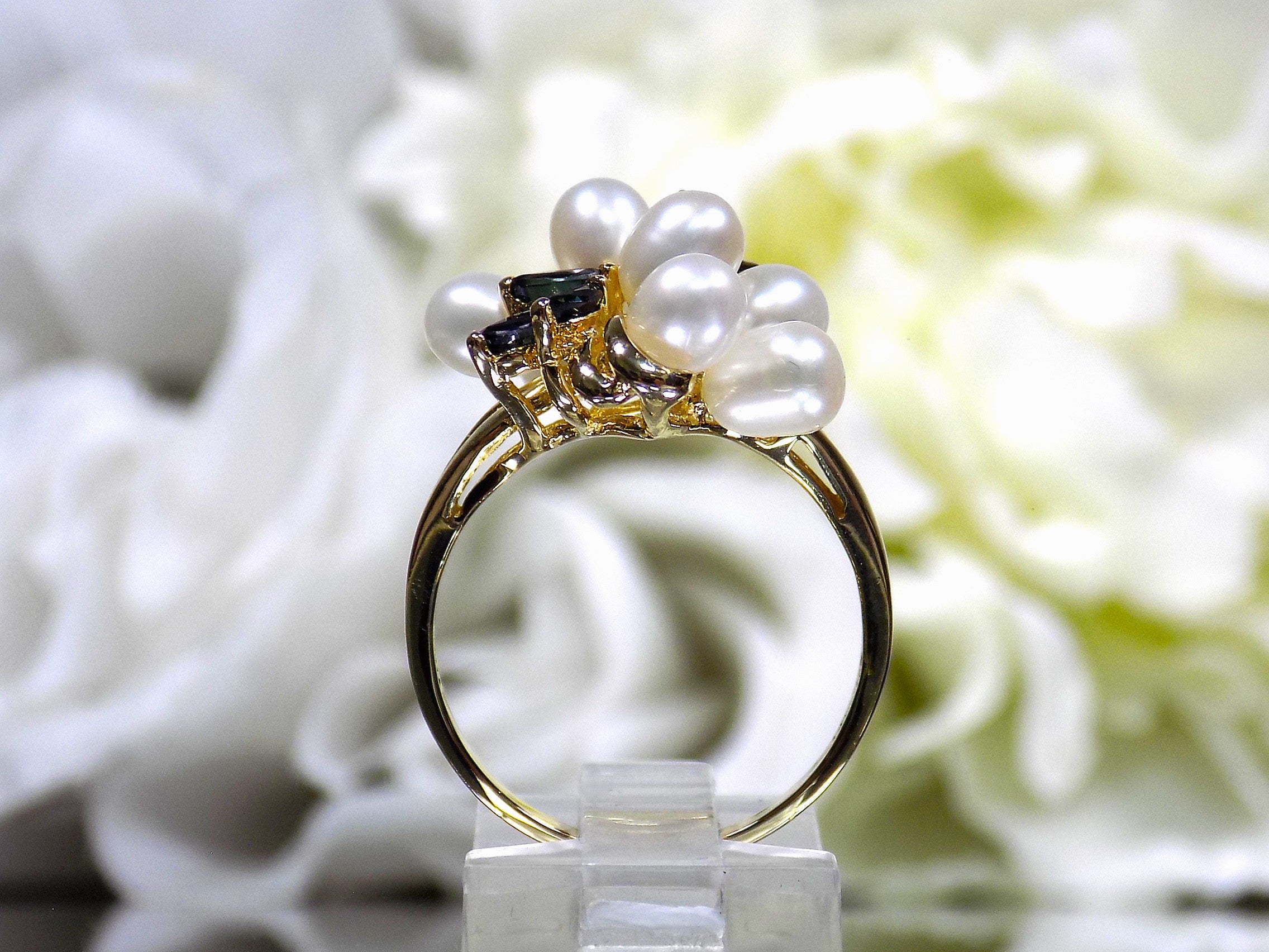 This is a side view of a freshwater pearl, blue sapphire, and diamond ring in yellow gold from our estate collection with a white flower background.