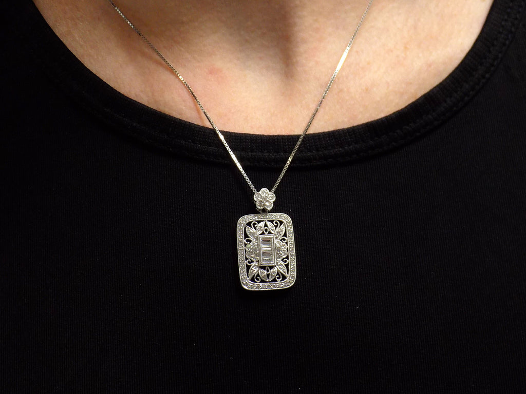 This is a Victorian style pendant with 1.00ct total weight round and baguette diamonds set in 900 platinum on a ladies neck with black shirt.