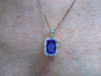 This is a women's 4.90ct natural high-end rectangular cushion cut tanzanite pendant surrounded by .75ct natural baguette and round diamond accents in 14K yellow gold on a women's neck.