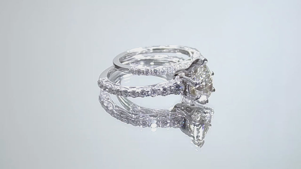 This is a video of a women's 2-piece wedding set including the engagement ring and a matching band with a 1.51ct natural pear shape diamond center plus 1.64ct in natural diamond accents shown rotating on a mirrored background.