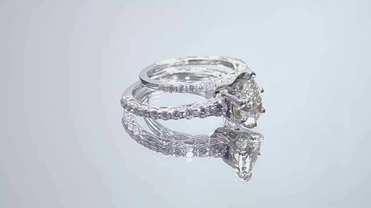 This is a video of a women's 2-piece wedding set including the engagement ring and a matching band with a 1.51ct natural pear shape diamond center plus 1.64ct in natural diamond accents shown rotating on a mirrored background.