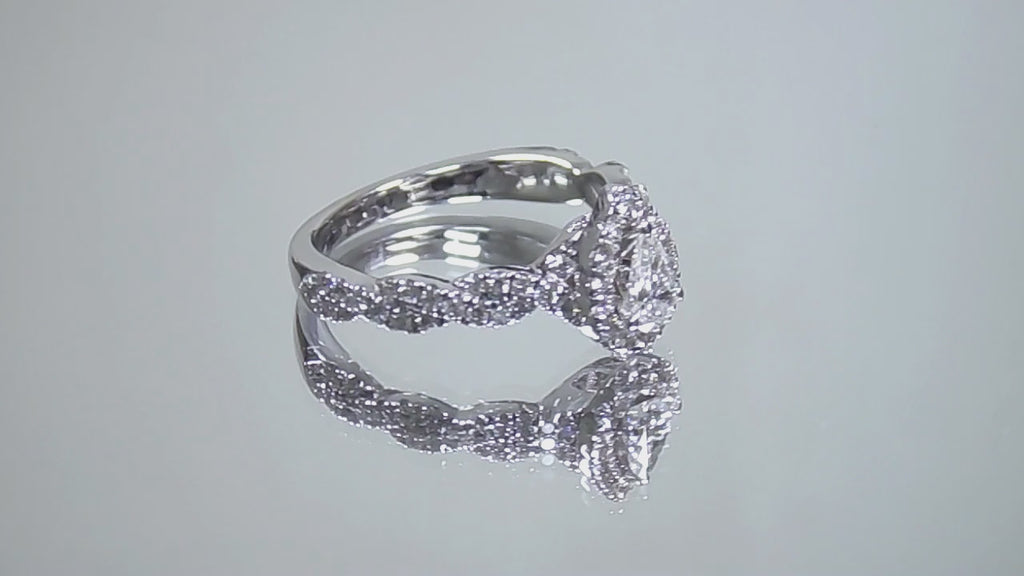 This is a video of a halo style .82ct total weight natural pear shape diamond ring with infinity style band in white gold shown turning slowly with a mirrored background.
