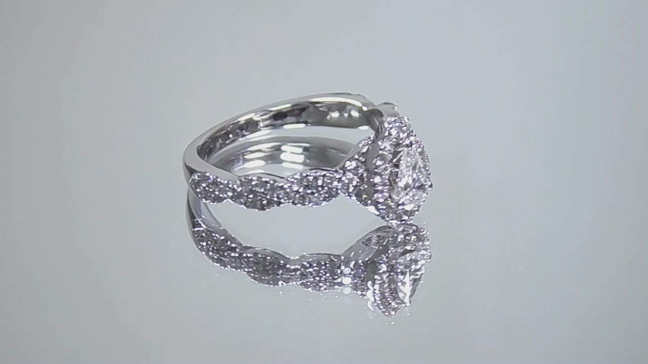 This is a video of a halo style .82ct total weight natural pear shape diamond ring with infinity style band in white gold shown turning slowly with a mirrored background.