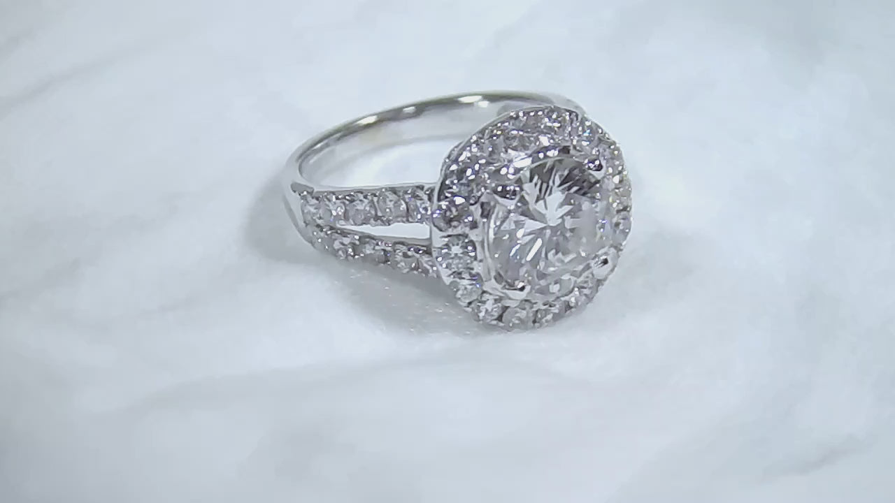This is a video of a 3.55ct total weight natural diamond ring with a 2.05ct natural round diamond center in white gold shown rotating slowly on a mirrored white background.