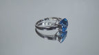 This is a tension set or channel set 4.00ct natural cushion cut blue topaz solitaire ring in 14K white gold on a mirrored surface rotating in a video.