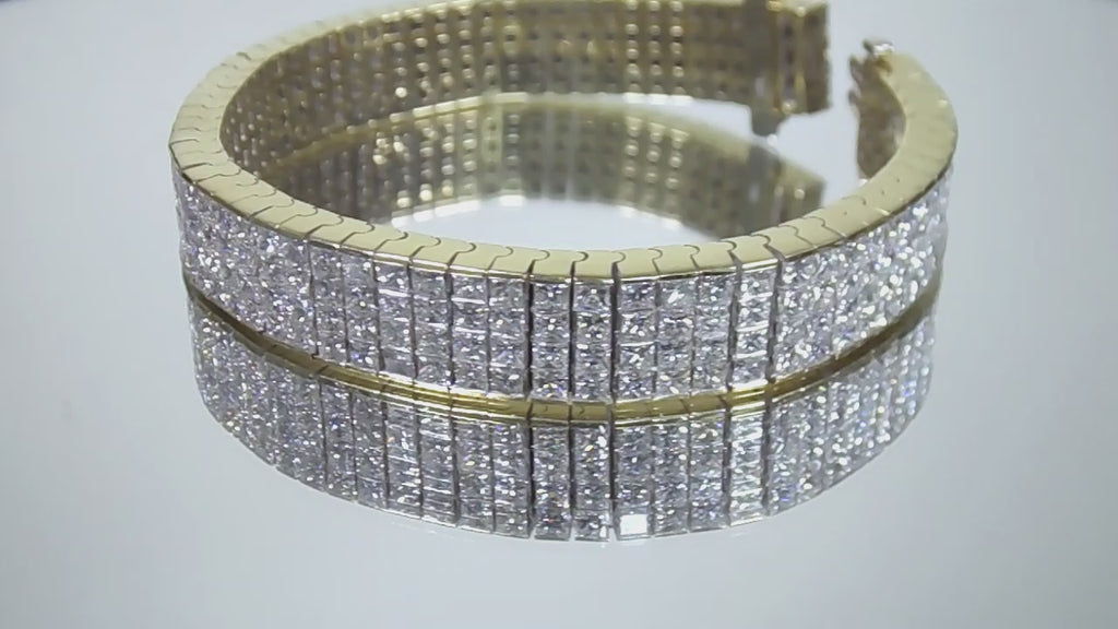 This is a 22.00ct natural princess cut diamond bracelet with 76.4 grams of 18K yellow gold on a mirrored surface rotating in a video.