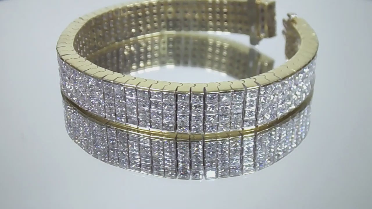 This is a 22.00ct natural princess cut diamond bracelet with 76.4 grams of 18K yellow gold on a mirrored surface rotating in a video.