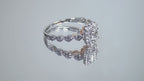 This is a video of a .75ct natural emerald cut halo style ring with infinity style band in white gold with rose gold accents on the sides turning slowly on a mirrored background.