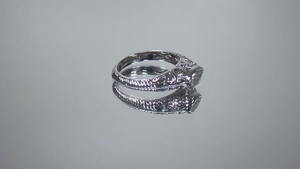 This is a bezel set marquise shape diamond set sideways in a white gold filigree ring shown turning slowly on mirrored background.
