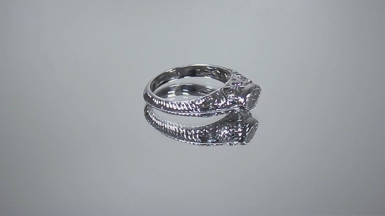 This is a bezel set marquise shape diamond set sideways in a white gold filigree ring shown turning slowly on mirrored background.