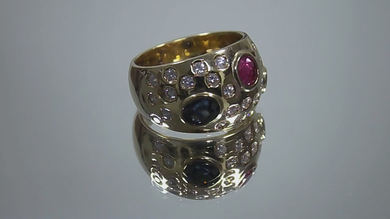 This is a women's estate ring with 2.50ct total weight ruby, sapphire, and diamonds set in 18K yellow gold on a mirrored surface rotating in a video