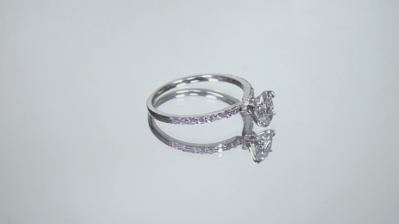 This a video of a 1ct total weight natural oval shape diamond set on a straight line diamond band in white gold shown turning slowly around on a mirrored white background.