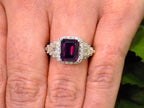 This is a woman's 3.95ct total weight rhodolite garnet and diamond ring in white gold shown on a woman's finger.