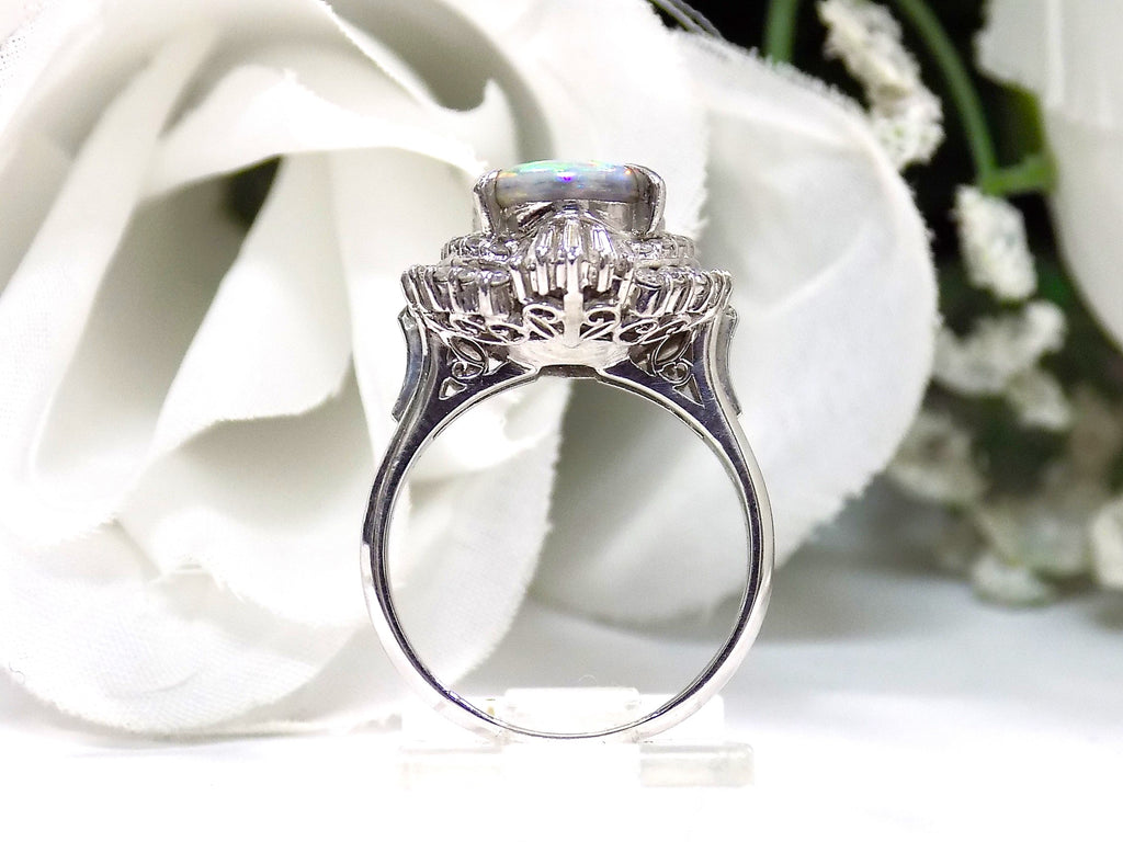 This is a women's ring with 2.51ct lightning ridge natural opal surrounded by .72ct natural baguette and round diamonds in 14K white gold with a white floral background from a side view.